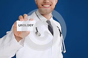Male doctor holding card with word UROLOGY on background, closeup
