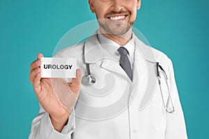 Male doctor holding card with word UROLOGY on turquoise background