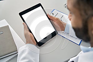 Male doctor holding digital tablet in hands looking at white mockup screen.