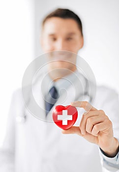 Male doctor holding heart with red cross symbol