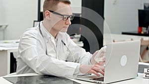 Male doctor holding jar of pills and typing prescription on laptop