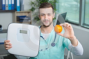 Male doctor holding orange and scale