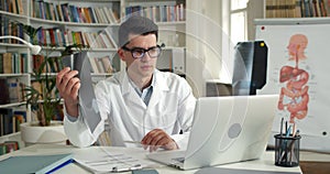 Male doctor holding x ray photo of chest while having online medical consultation in office.Young man in glasses and