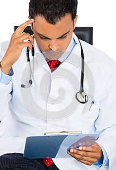 Male doctor in lab coat holding reading Patients Chart while sitting on a chair