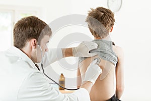 Male doctor listening boy back with stethoscope