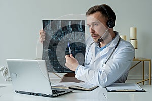 Male doctor listening to patient during telemedicine session. Man doctor having online consultation on laptop holding x