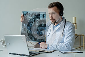 Male doctor listening to patient during telemedicine session. Man doctor having online consultation on laptop holding x