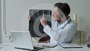 Male doctor listening to patient during telemedicine session. Man doctor having online consultation on laptop holding x