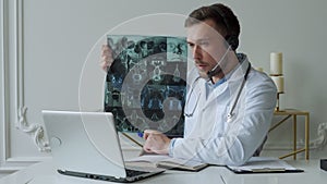 Male doctor listening to patient during telemedicine session. Man doctor having online consultation on laptop holding x