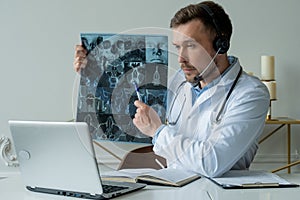 Male doctor listening to patient during telemedicine session. Man doctor having online consultation on laptop holding x