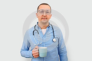 Male doctor looking at the camera with a cup in his hands on a gray background.