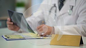 Male doctor looking at lungs x-ray, writing diagnosis, blank nameplate on table