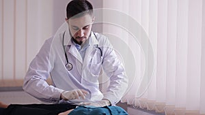 Male doctor makes palpation of the abdomen of the patient. The girl lies on a couch in the doctor`s office.