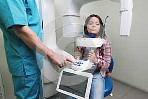 A male doctor makes an x-ray of the girl`s jaw, which sits in a special X-ray machine. The girl is smiling.