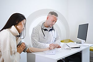 The male doctor measures the woman blood pressure and records the results in the patient`s card.