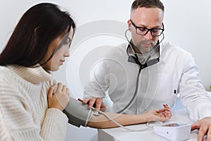 Male doctor at the medical examination measures the blood pressure of a woman patient.