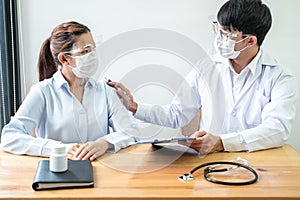 Male doctor in medical mask is hold patient shoulder to encourage and explaining treatment after writing prescription