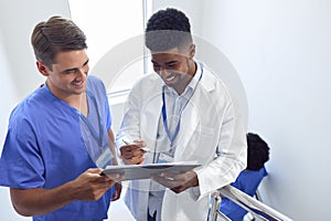 Male Doctor And Nurse Discussing Patient Notes On Stairs In Hospital Building