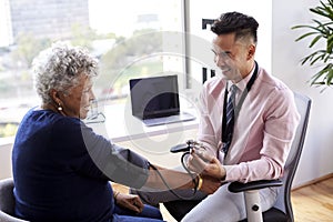 Male Doctor In Office Checking Senior Female Patients Blood Pressure