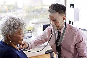 Male Doctor In Office Listening To Senior Female Patients Chest Using Stethoscope