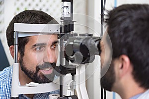 Male doctor ophthalmologist is checking the eye vision of handsome young man in modern clinic. Doctor and patient in