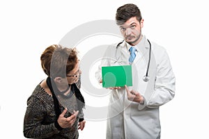 Male doctor pointing on green board to female senior patient