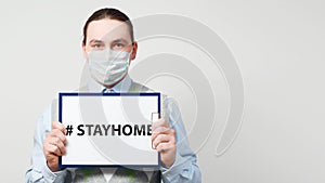Male doctor in protective mask is holding paper with the hashtag stayhome