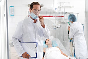 Male doctor pulling off protective mask while holding clipboard and pen