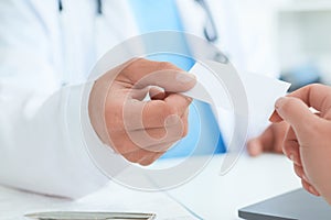 Male doctor`s hand give white blank calling card to woman closeup in office. Physical, disease prevention, examine