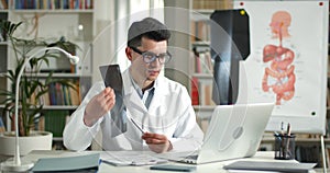 Male doctor showing x ray photo to patient while having online medical consultation in office. Man in glasses and white