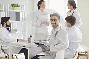 Male doctor sitting at a table with collegues in white lab coats at a medical hospital.
