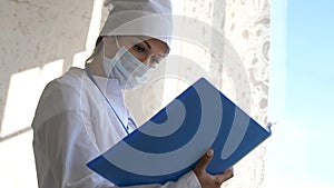 Female Doctor in medical mask standing with folder looks at the medical history photo