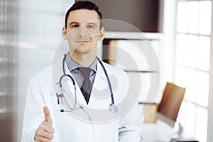 Male doctor standing with thumbs up sign in sunny clinic. Perfect medical service in hospital