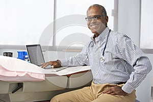 Male Doctor In Surgery Using Laptop