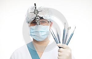 Male doctor in a surgical mask with binocular loupes and holding dental instruments
