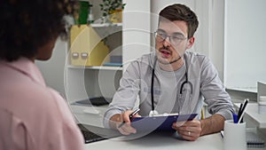 Male doctor talking to female patient and giving advice, sitting at table in clinic office spbd.