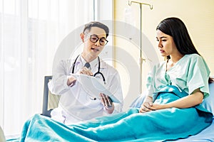 Male doctor talking to Female patient in hospital bed, while pointing notes on clipboard, Medicine and health care concept,