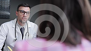 Male doctor talking to female patient and writing while sitting at table in modern clinic spbi.