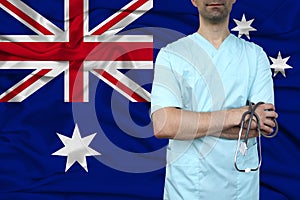 Male doctor in uniform professional clothes with a stethoscope stands against the background of the national flag, the concept of