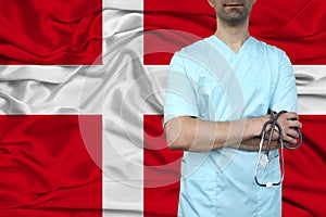 Male doctor in uniform professional clothes with a stethoscope stands against the background of the national flag, the concept of