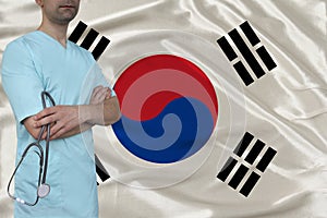 Male doctor in uniform professional clothes with a stethoscope stands against the background of the national flag, the concept of