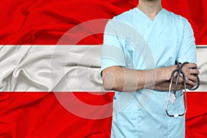 Male doctor in uniform professional clothes with a stethoscope stands against the background of the national flag, the concept of