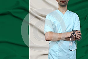 Male doctor in uniform professional clothes with a stethoscope stands against the background of the national flag, the concept of