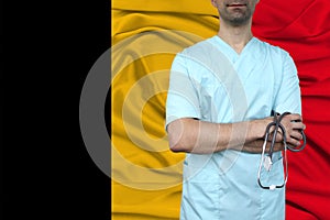 Male doctor in uniform professional clothes with a stethoscope stands against the background of the national flag, the concept of