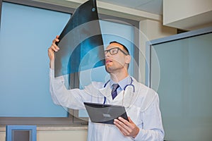 Male doctor in uniform with tablet computer looking at the x-ray picture of spinal column in hospital.