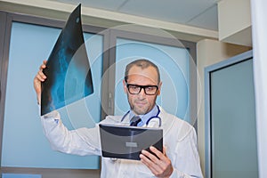 Male doctor in uniform with tablet computer looking at the x-ray picture of spinal column in hospital.