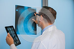 Male doctor in uniform with tablet computer looking at the x-ray picture of spinal column in hospital.