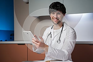 Male doctor using a digital tablet in a clinic. A successful smiling doctor in a lab coat with a stethoscope.