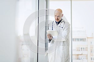 Male doctor using digitla tablet while standing on clinic`s foyer