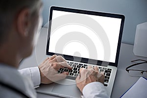 Male doctor using laptop computer with blank white mockup screen technology.